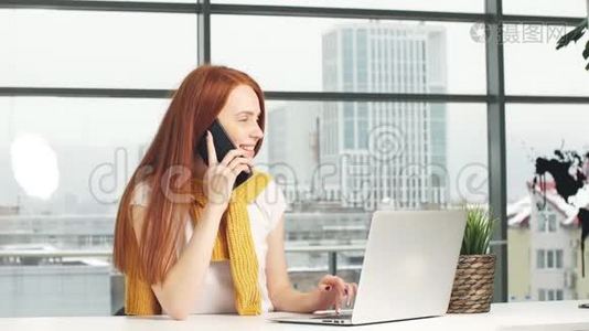 快乐的红头发女孩，在办公室工作，使用笔记本电脑和手机。视频