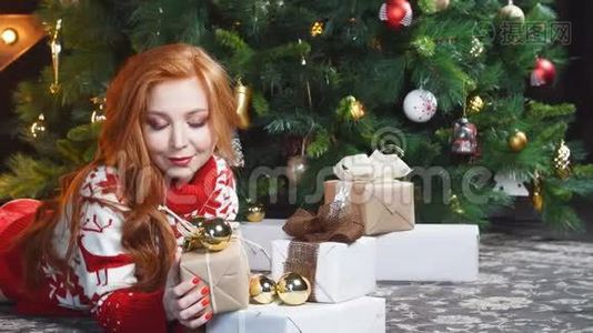 漂亮的红发女孩穿着红色毛衣躺在地上，带着礼品盒。视频