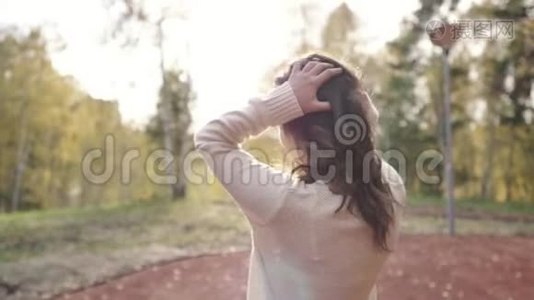 一个穿毛衣的年轻女子在秋天公园散步。 黑发女人在寒冷的森林里晒太阳。 公园里的浪漫女人视频