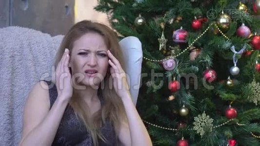 在圣诞树背景上头痛的被压着的女人。 室内悲伤的年轻女子视频