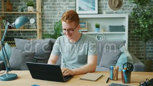 年轻的男性自由职业者在家工作，使用笔记本电脑打字和微笑视频