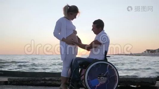 残疾人和妻子在晚上跳舞，残疾配偶在轮椅上，孕妇在日落时跳舞视频