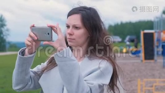 年轻女子在操场上用手机拍摄照片和视频。视频