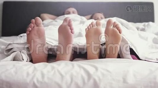 年轻可爱的快乐夫妇在毯子下玩耍和跳舞，而早上醒来在床上。 慢动作视频