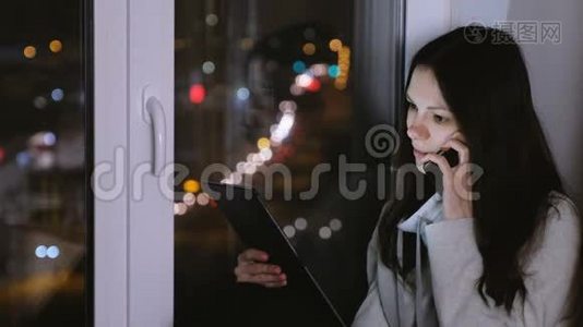 女人在手机上说话，看着平板电脑。 夜深人静的坐在窗台上..视频