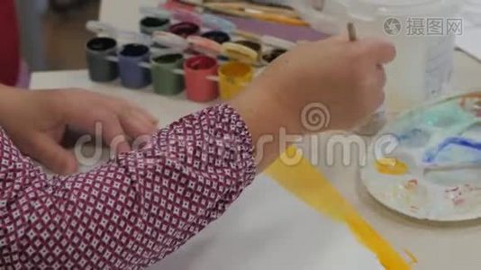 艺术家在画布纸上画一条黄色的画，艺术家在工作室里，造物主做一个刷子的运动。视频