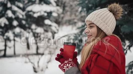 年轻漂亮的女孩穿着暖和的衣服站在圣诞树旁边，在雪地里喝着报纸上的热饮料视频