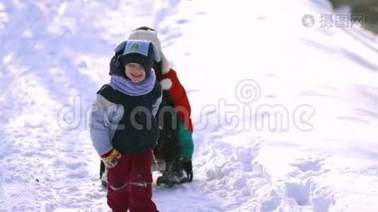 妈妈和小儿子在雪地里玩得很开心。 他们坐雪橇。视频