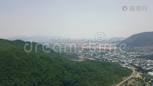 从青山和小山到远处的现代城市的空中镜头。 绿色道路和乡村房屋视频