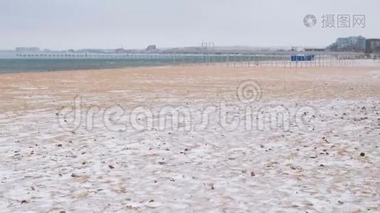 冬天的雪在海沙滩上，背景是沿海城镇。视频