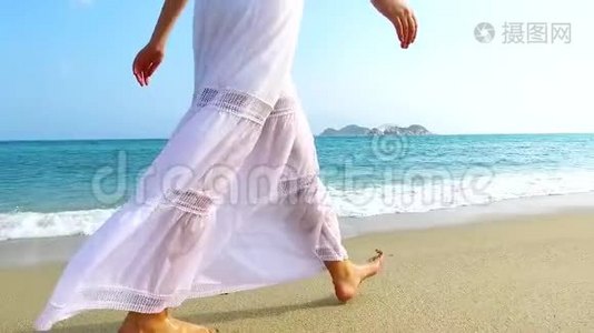 阳光明媚的一天，穿着白色连衣裙的女孩在沙滩上散步。 慢动作。视频