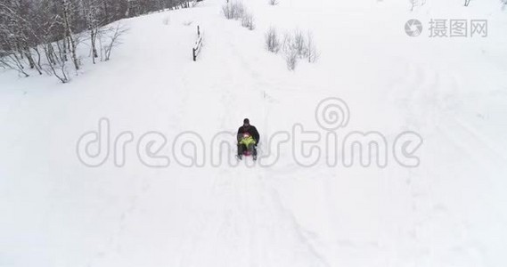 冬天的空中跟随父亲骑着红色的雪橇和孩子在下雪的下坡。 爸爸，儿子或女儿，斯诺的雪橇视频