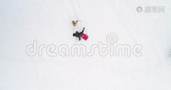 冬天的头顶俯视着父亲拉着红色的雪橇和孩子一起飞升。 爸爸，儿子或女儿，瑞雪视频