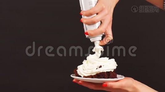 特写女手糖果师将鲜奶油倒在纸杯蛋糕上。视频