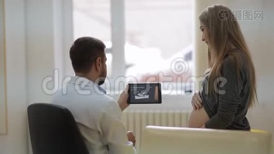 一位身穿白色医用晨衣的医生在平板电脑上展示了一位孕妇的超声波照片视频