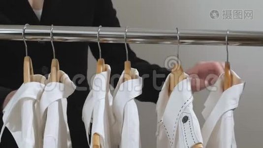 穿黑色夹克的女人会选择挂在衣柜或商店衣架上的白色衬衫视频