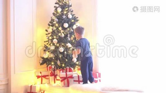 可爱的小男孩用球和灯装饰圣诞树。在家里准备过年的孩子。视频