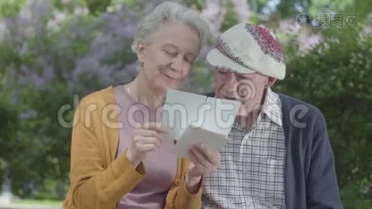 成年男女看着老照片，回忆着坐在公园长凳上的快乐时刻。 成熟的情侣相爱视频