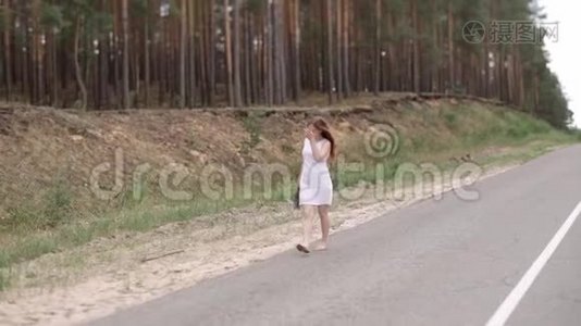快乐的女孩穿着一件白色的连衣裙，手里拿着一束花，赤脚在路上行走。视频