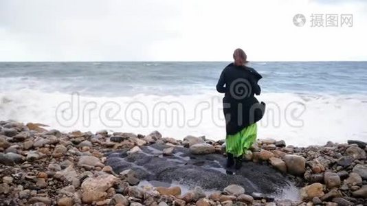 穿着黑色衣服的女人从海里跑出来，溅起水花，笑了起来。 多云风天气。视频