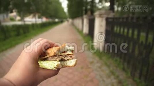 一个男人正在街上吃快餐，手里拿着一个汉堡包。视频