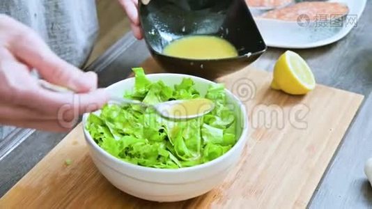 家庭厨房中的女性手的特写被添加到素叶沙拉酱中，并在木制的勺子上混合视频