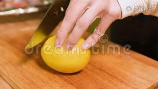 在家厨房的一个女孩的手在一个木切割板上特写。 在婴儿车上切一个黄柠檬。 家庭视频