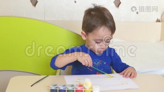 坐在桌子旁的一张白纸上，孩子用水彩作画。视频