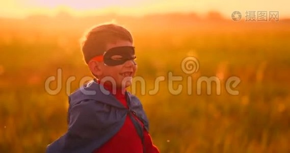 一个戴着面具的男孩和一个超级英雄在日落时在田野里的斗篷视频