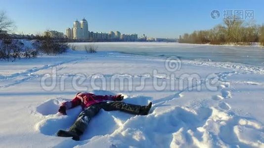 快乐的小女孩躺在城市公园的雪地上。 玩雪。 寒假快乐视频