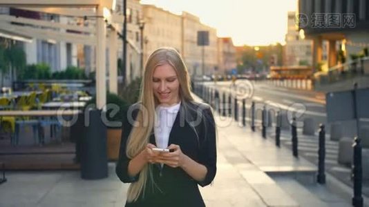 正式的女商人在街上散步。 优雅的金发女郎穿着西装，走在街上，用智能手机浏览视频