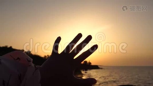 女孩在黎明时分的海上与升起的太阳玩耍。 处理手指间的太阳射线。视频