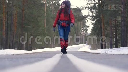 年轻女子背着背包在美丽的冬林中徒步，走在柏油路上..视频