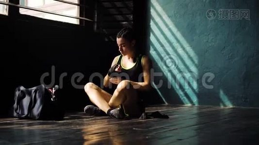 惊慌失措的年轻美女坐在地板上，用黑色拳击包裹在俱乐部里的手。视频