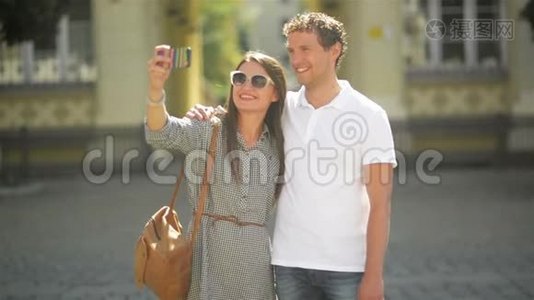 在阳光明媚的夏日，年轻夫妇在城市广场上使用智能手机站立户外活动。视频