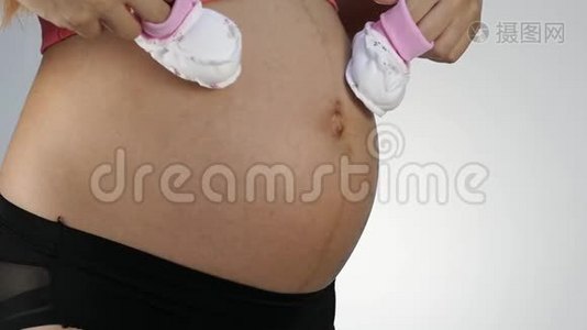穿着内衣的孕妇在肚子上玩婴儿鞋。 慢动作视频