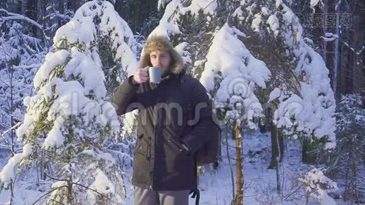 一个年轻人在冬天的森林里喝热茶。 冬天森林里阳光明媚的早晨。 那个人看了看视频