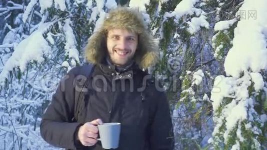一个年轻人在冬天的森林里喝热茶。 冬天森林里阳光明媚的早晨。 那个人看了看视频