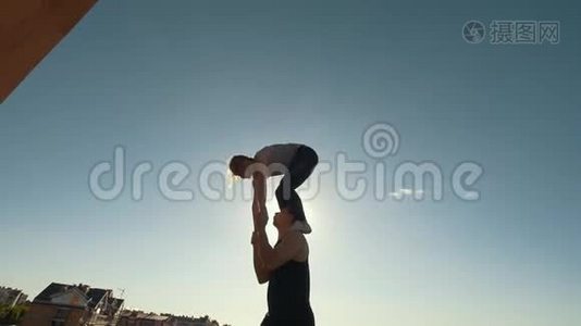 年轻的杂技演员夫妇表演翻转动作，年轻人在户外日落时把一个女人抛在空中平衡的手臂上视频