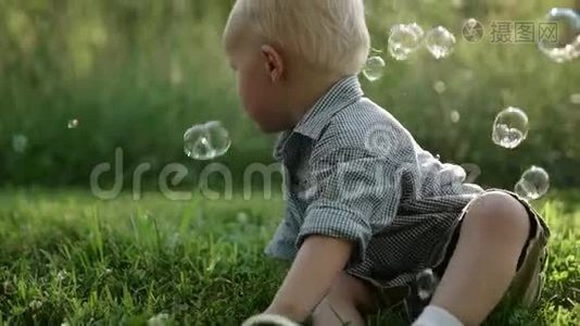 小男孩坐在草地上，户外玩肥皂泡，慢动作，全高清视频