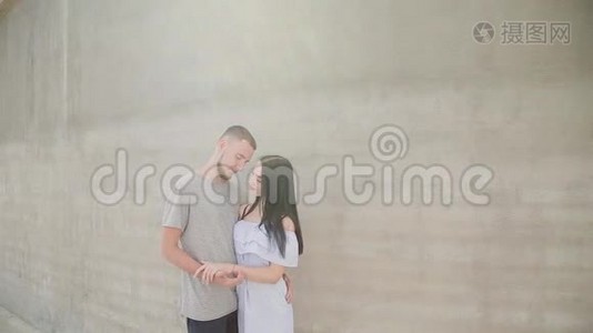 一对相爱的夫妇在混凝土墙的背景下拥抱和亲吻。视频