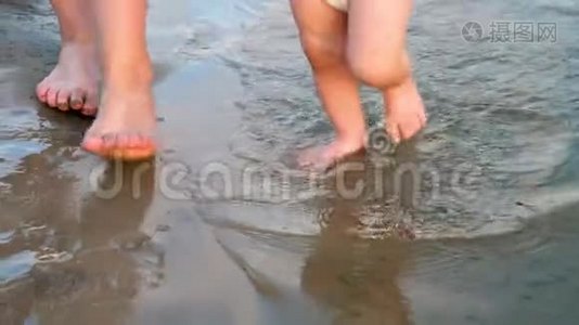 宝贝沿着河岸走第一步，在两边泼水，和他妈妈一起走。 腿。 特写镜头。 慢慢视频
