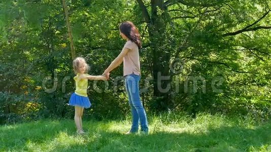 在公园里，穿着粉色衬衫的年轻母亲和穿着牛仔裤旋转可爱的小女儿的户外画像视频