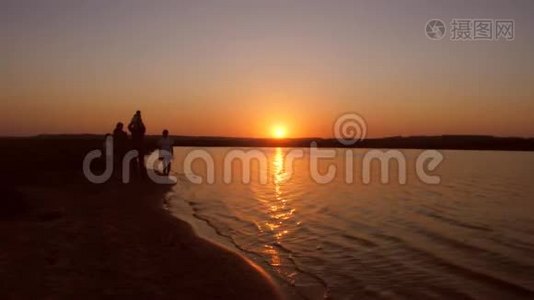 一家人在夕阳红下沿着海岸散步。 慢动作。视频
