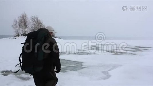 背着背包的人在融化的河面上的暴风雪中行走视频