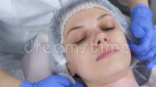 美容师用棉垫擦拭一个年轻女人的脸。 美容师戴手套和面部特写视频