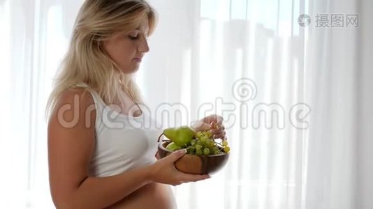 怀孕期间的饮食，大肚子的女孩拿着装有水果的木盘吃葡萄视频