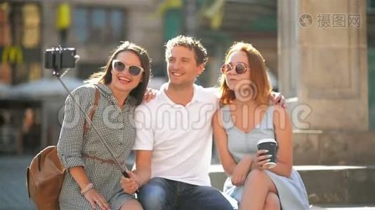 阳光明媚的夏日，三位快乐的朋友在城市广场的智能手机户外自拍视频