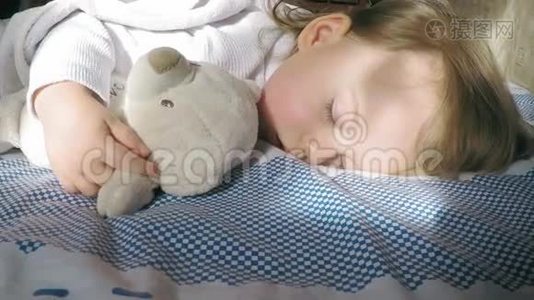 可爱的小女孩，金发睡在床上，被太阳照亮，带着泰迪熊视频