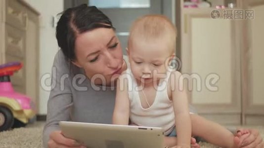 年轻的母亲和小男孩在地板上的地毯上玩平板电脑。 妈妈和儿子玩数字平板电脑视频